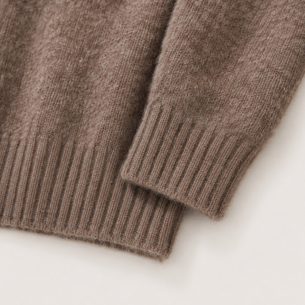 Close-up of a ribbed knit sweater sleeve in a warm taupe-brown color, showing the soft texture and ribbed cuff on a light neutral background.